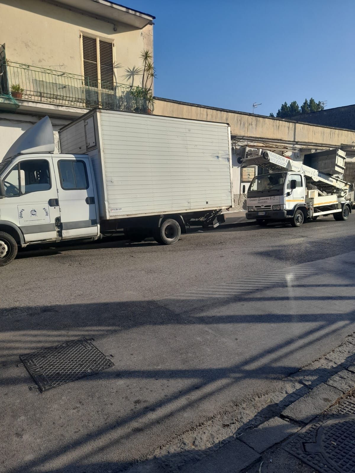 Due camion bianchi parcheggiati su una strada asfaltata di fronte a un edificio.