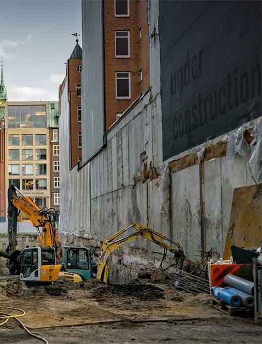 Construction site with excavators in front of a tall building.