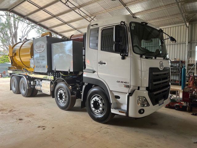 White and yellow vac truck parked inside a large open garage.