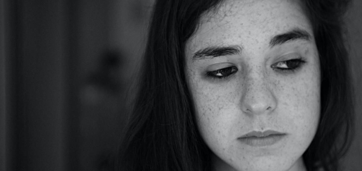 A black and white photo of a young girl with freckles looking down.