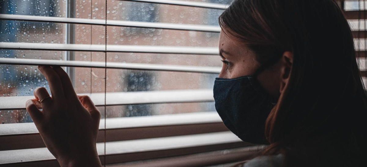 A woman wearing a mask is looking out of a window.