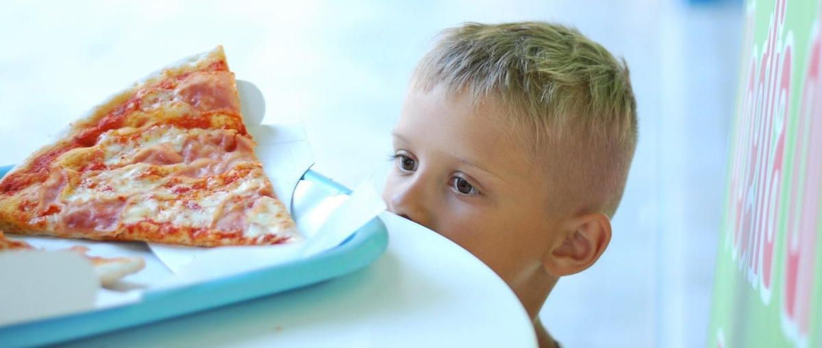 A young boy is eating a slice of pizza from a box.