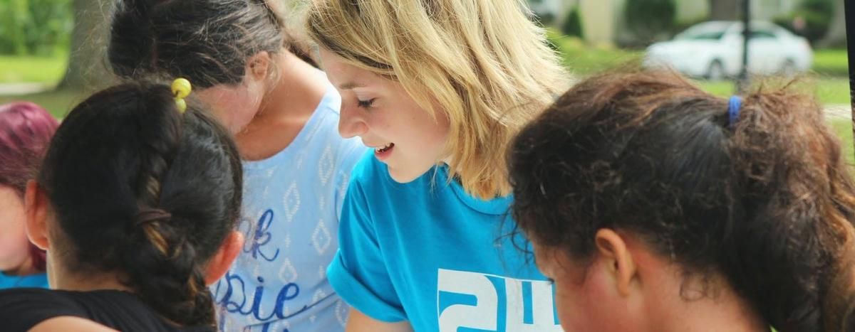 A woman in a blue shirt is talking to a group of children.