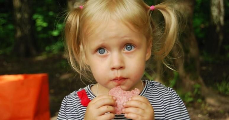 A little girl is eating a piece of meat.