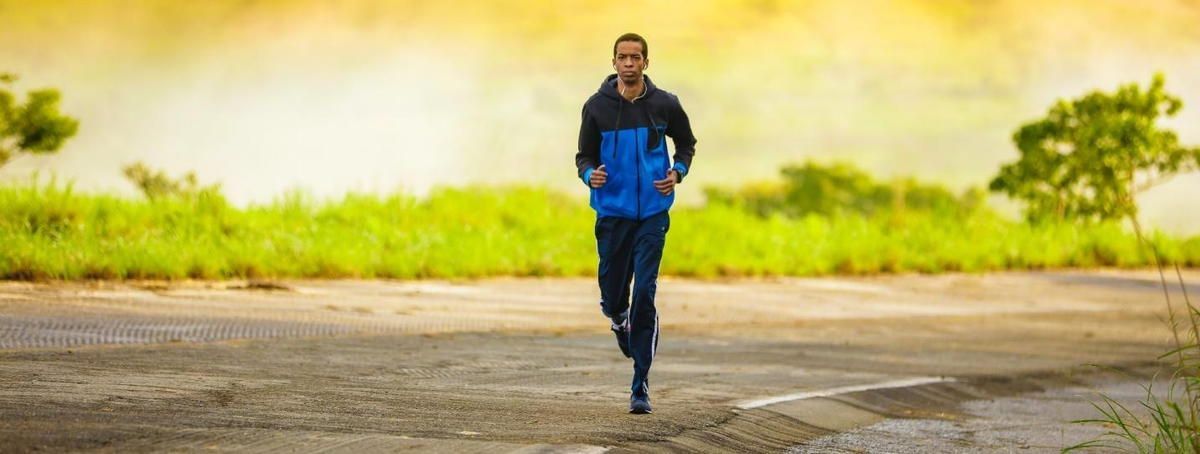 A man in a blue jacket is running down a road.