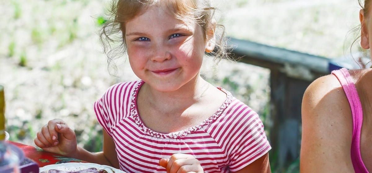 A little girl is sitting at a table eating a piece of cake.