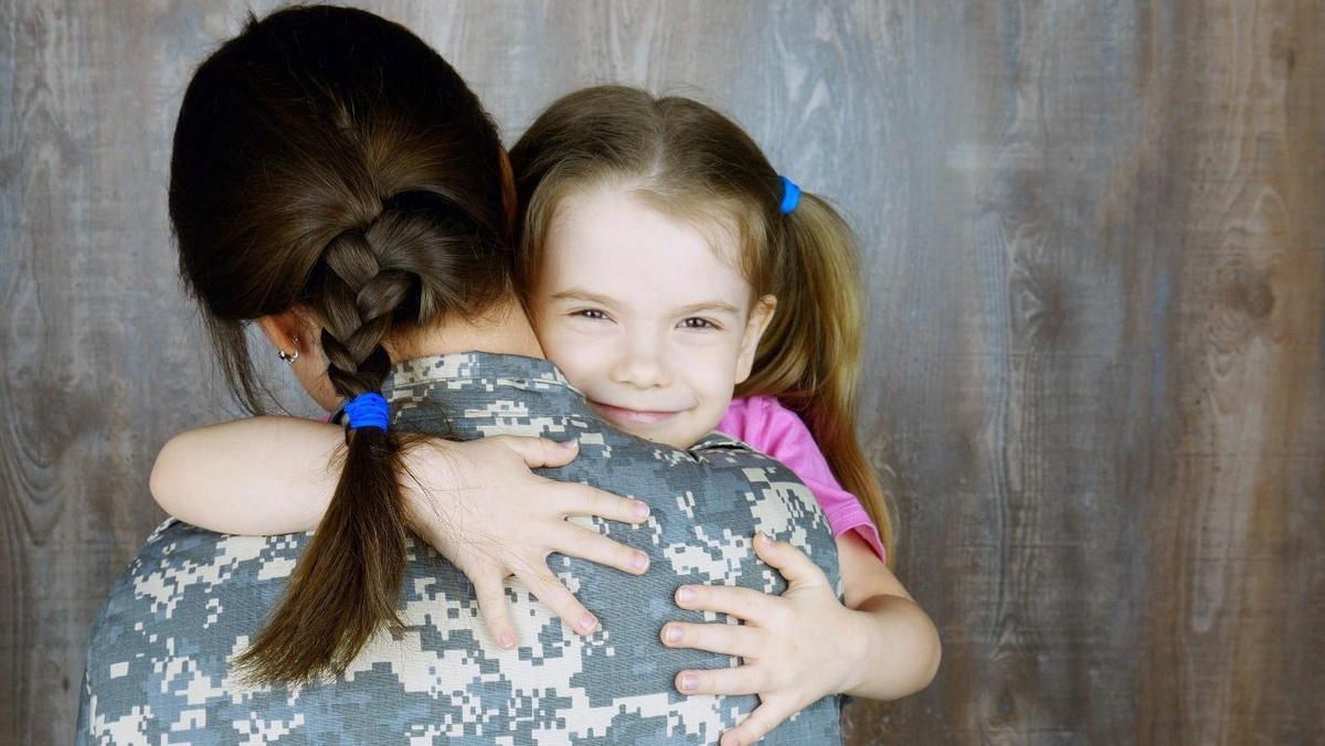 A woman in a military uniform is hugging a little girl.