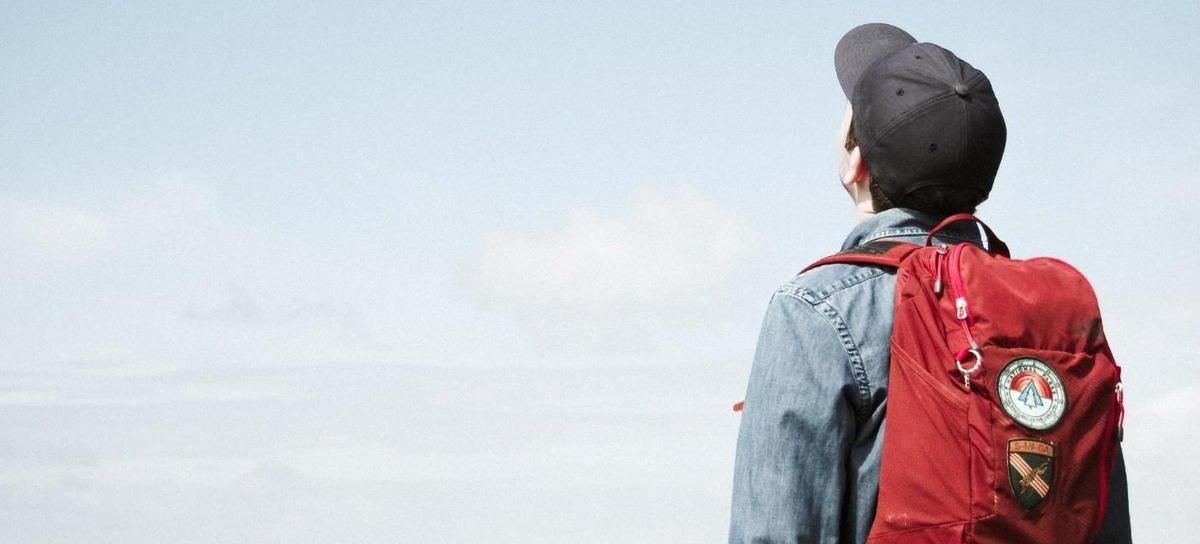 A man with a red backpack is looking at the sky.