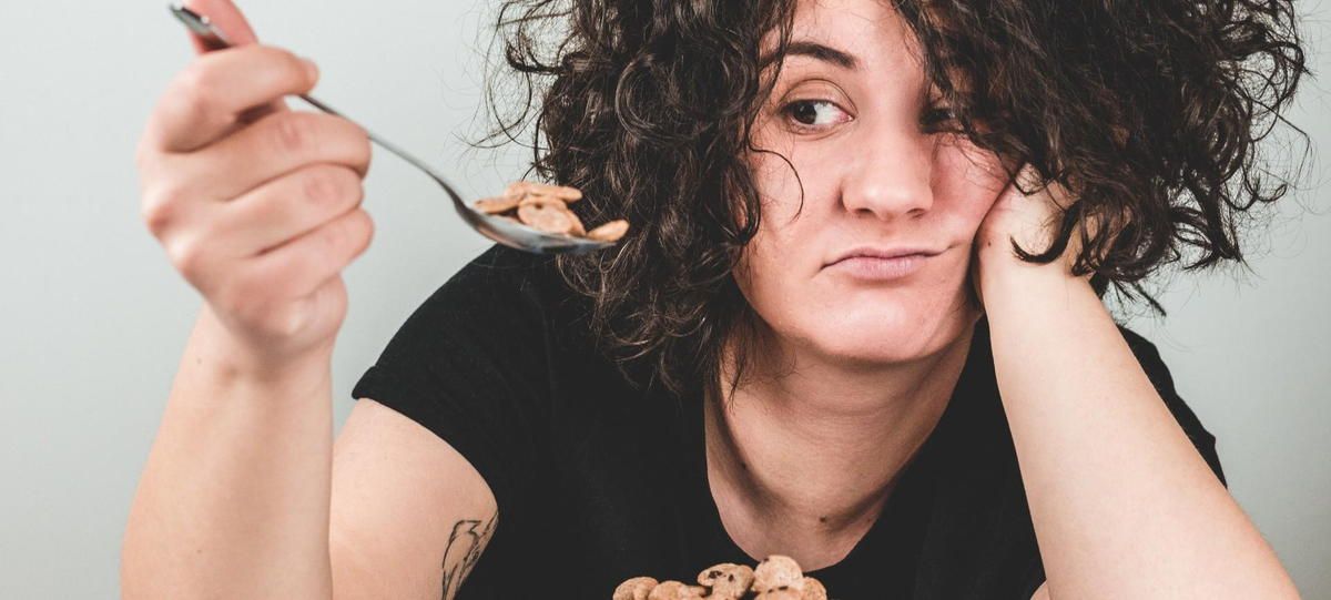 A woman with curly hair is eating cereal with a spoon.