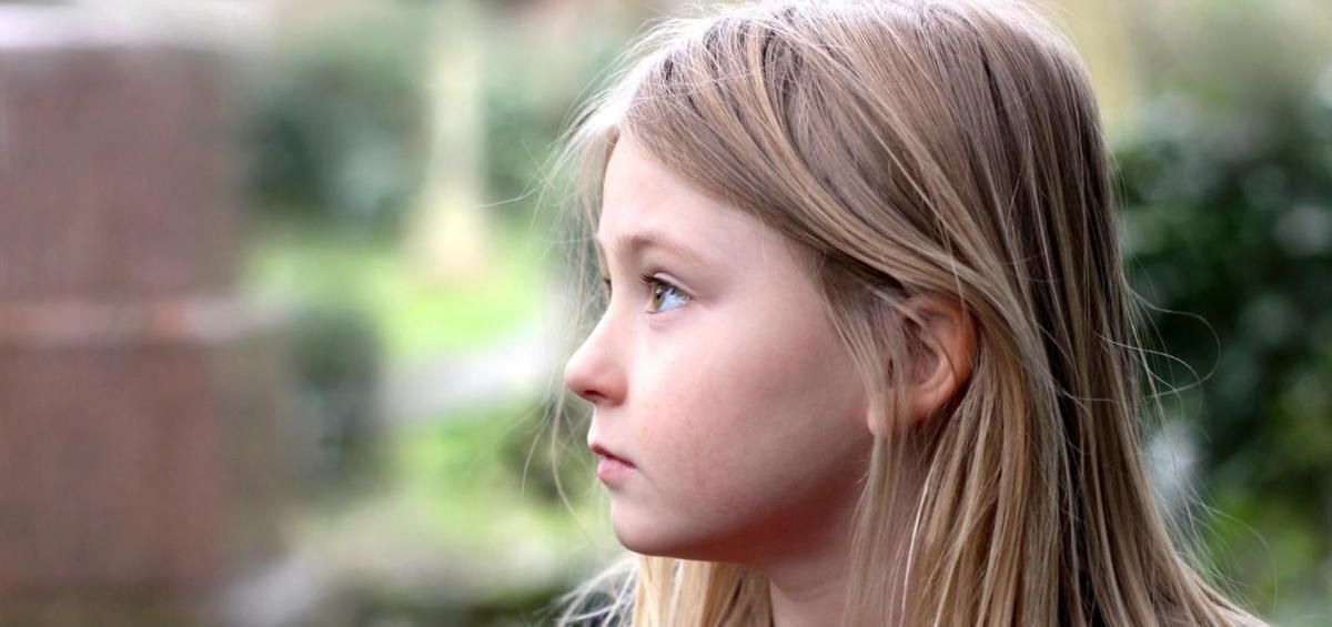 A young girl with long blonde hair is looking to the side.