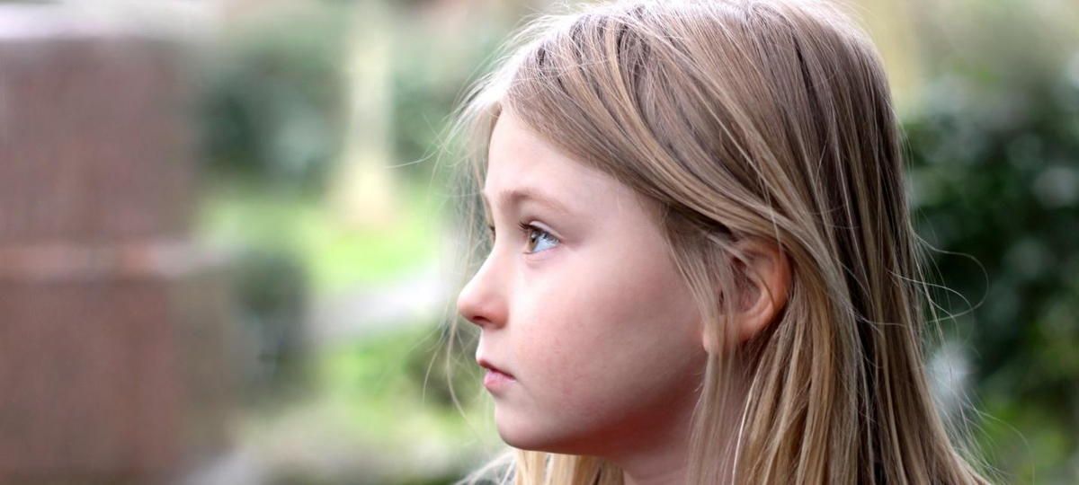 A young girl with long blonde hair is looking to the side.