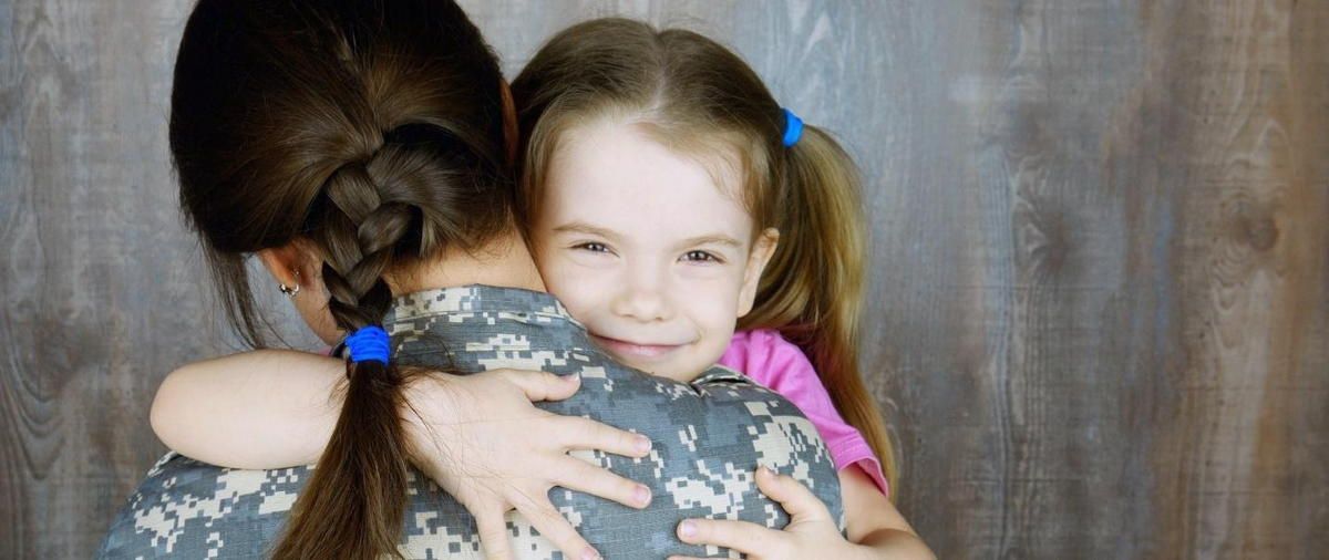 A woman in a military uniform is hugging a little girl.