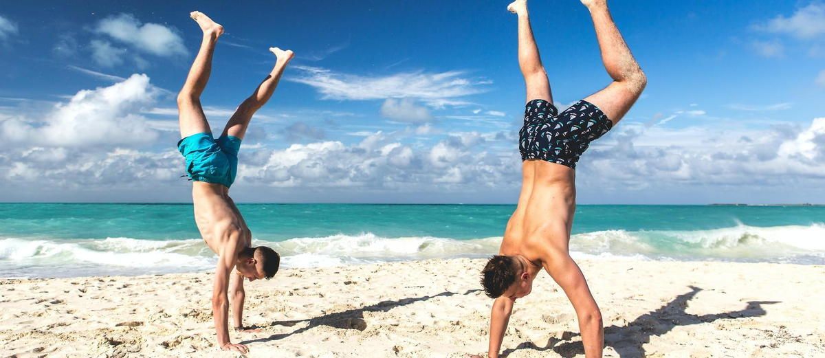 Two men are doing handstands on the beach.