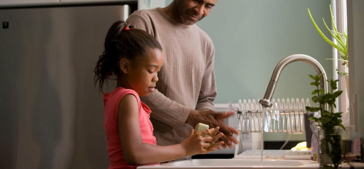 A man and a little girl are washing their hands in a kitchen sink.