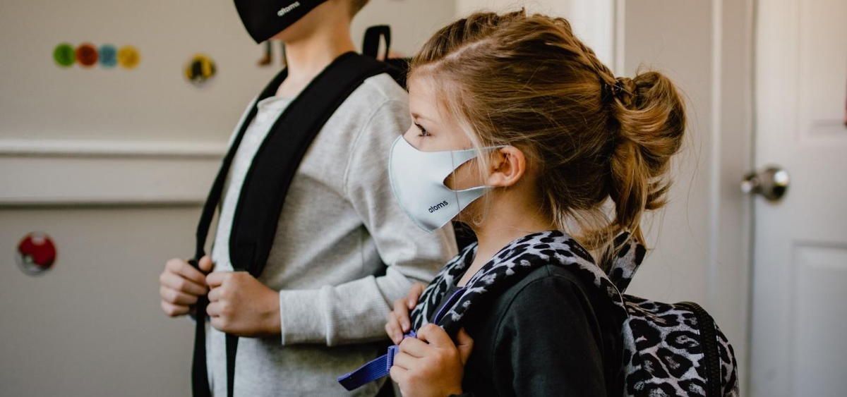 A boy and a girl wearing masks and backpacks are standing next to each other.