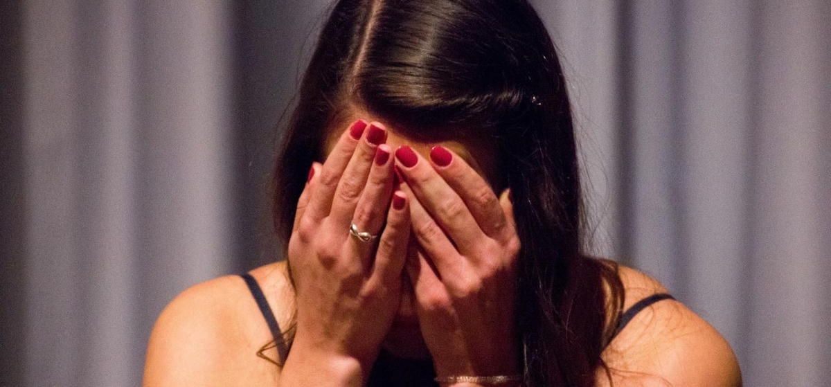 A woman with red nails is covering her face with her hands.