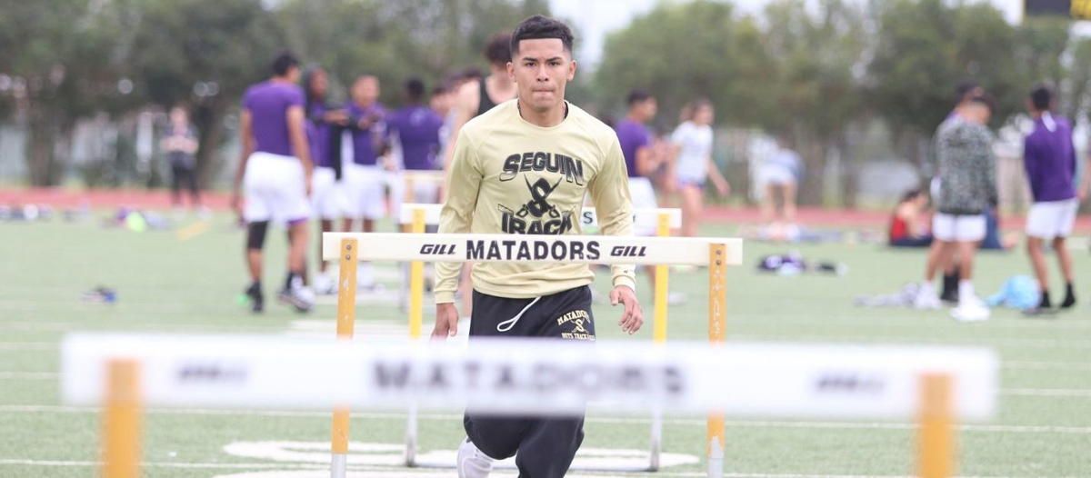 A man in a matadors shirt is jumping over hurdles on a field.