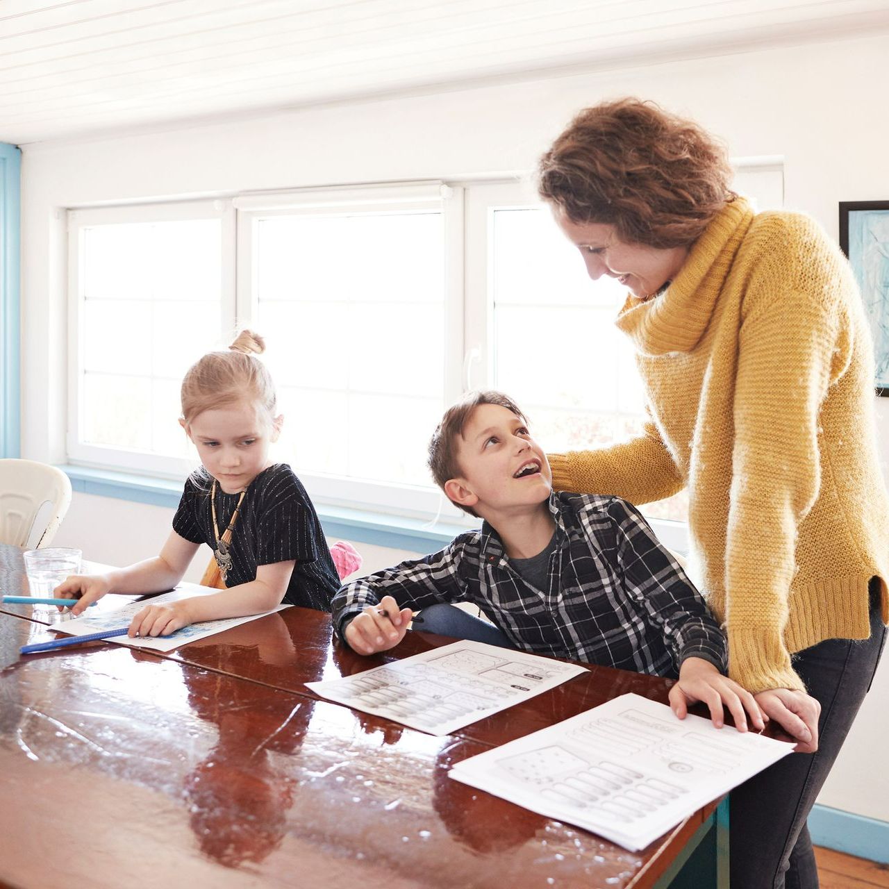 A woman in a yellow sweater is helping two children with their homework