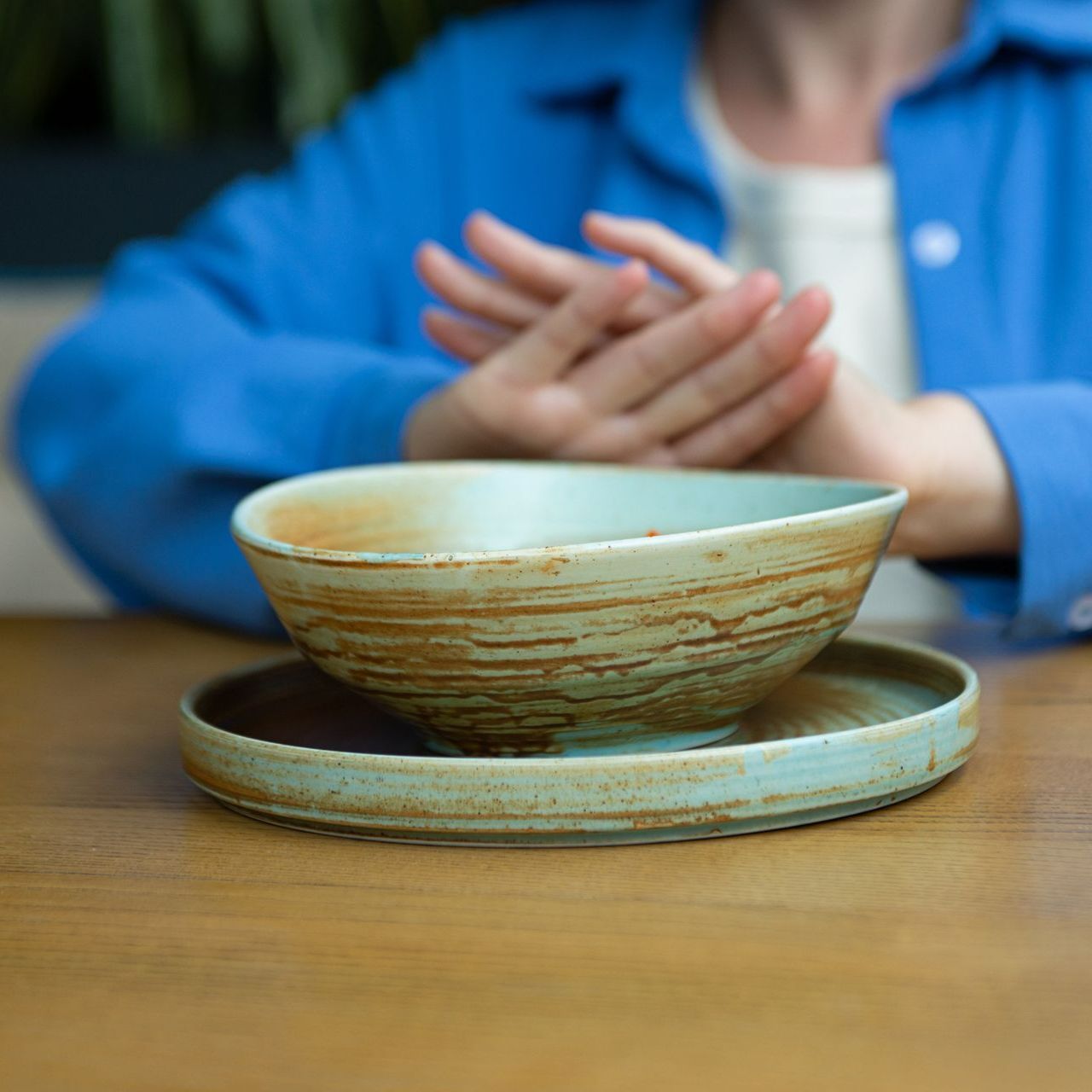 A woman in a blue jacket is sitting at a table with a bowl and plate