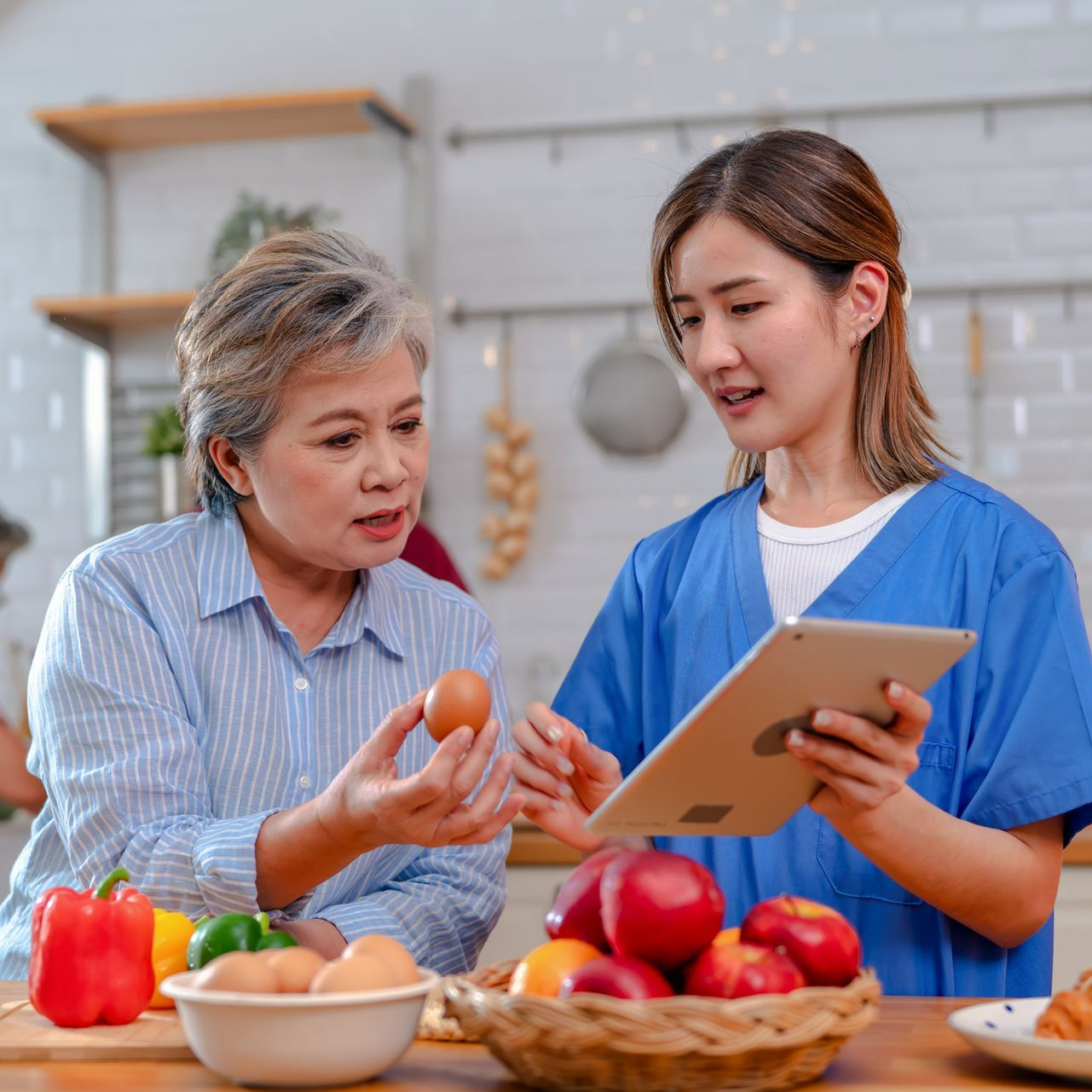 A nurse is showing an older woman how to cook on a tablet.