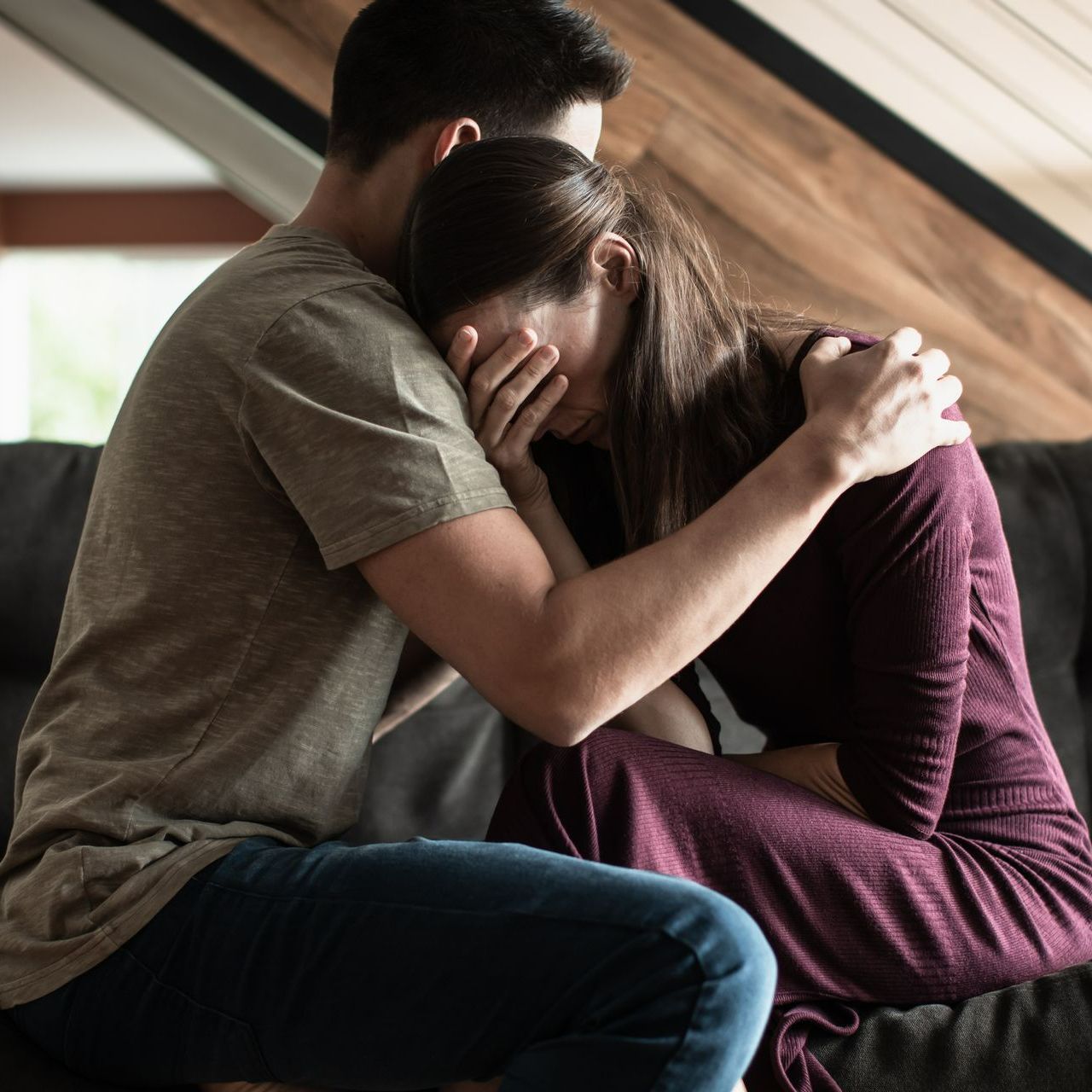 A man is comforting a woman who is sitting on a couch