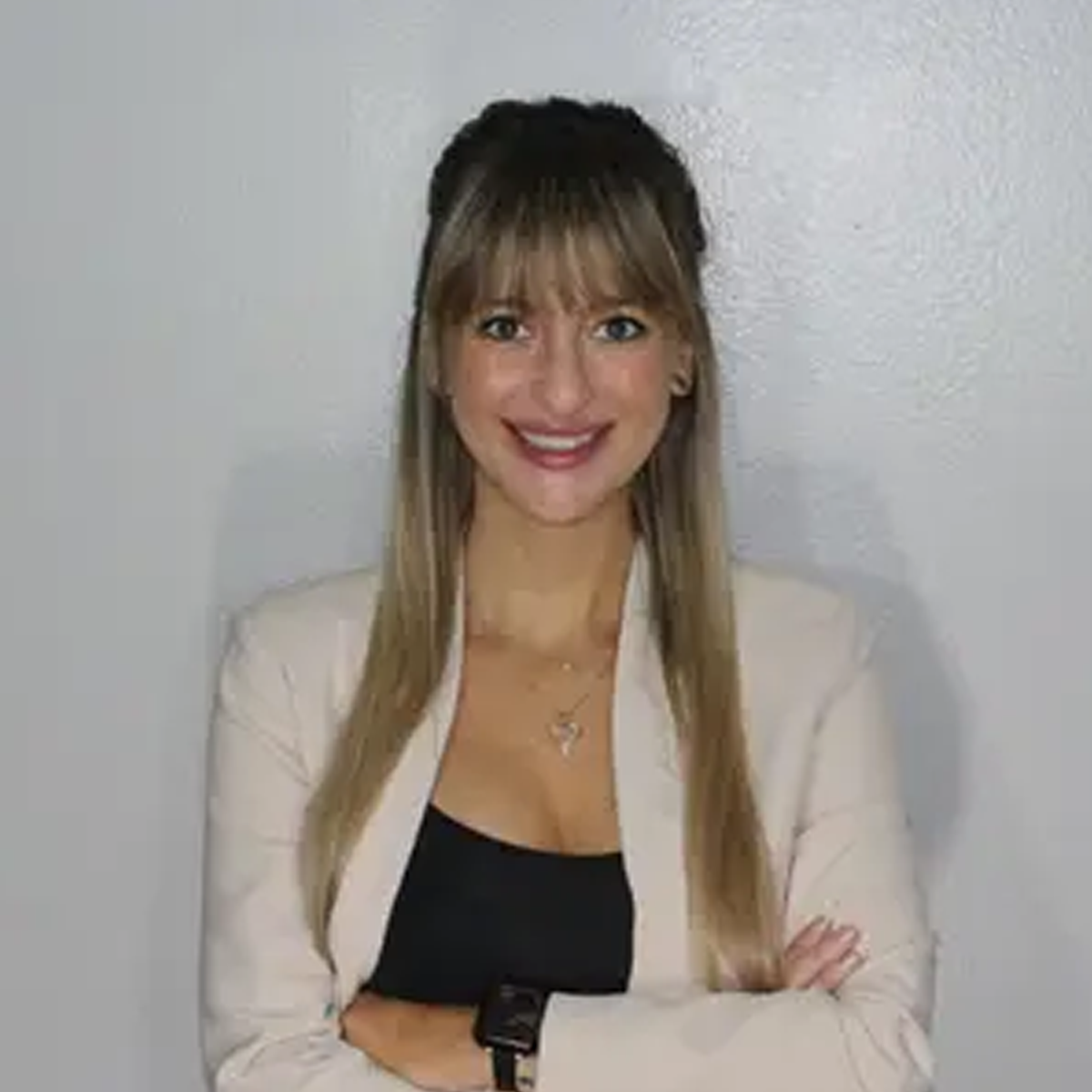 A woman in a white jacket and black top is standing with her arms crossed and smiling.