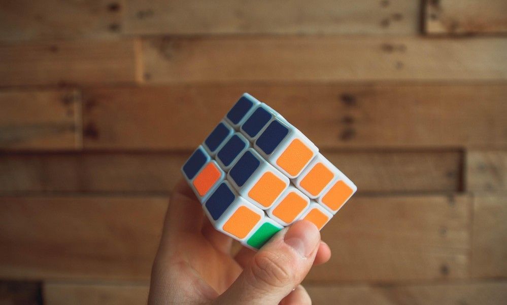 A person is holding a rubik 's cube in their hand in front of a wooden wall.