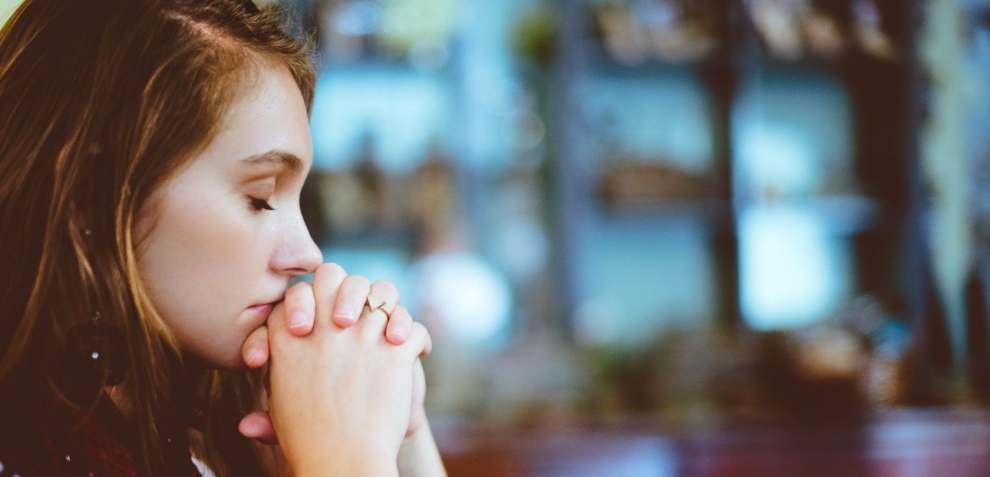 A young woman is praying with her hands folded in front of her face.