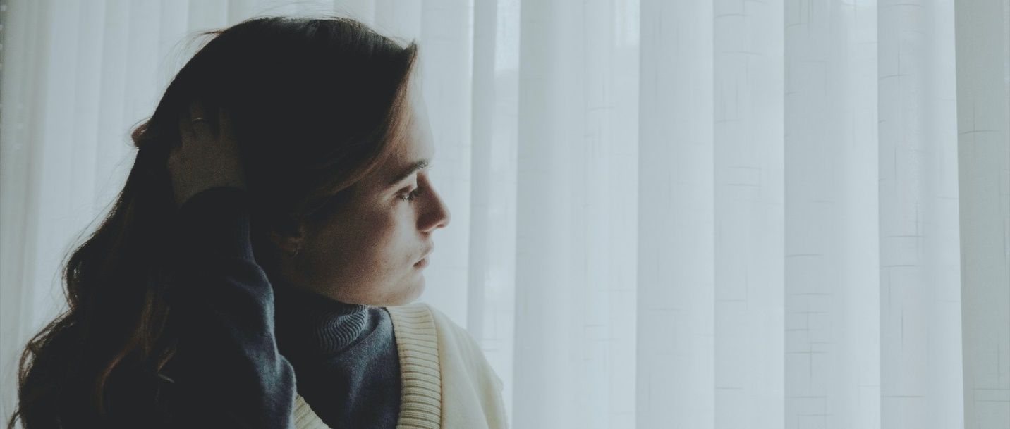 A woman is standing in front of a window looking out.