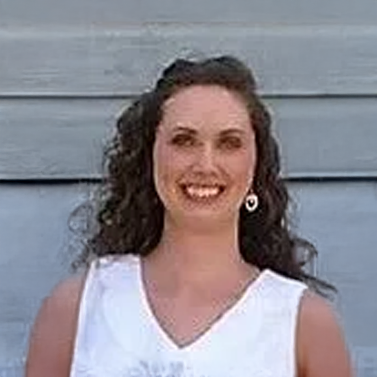 A woman wearing a white tank top and earrings is smiling for the camera.