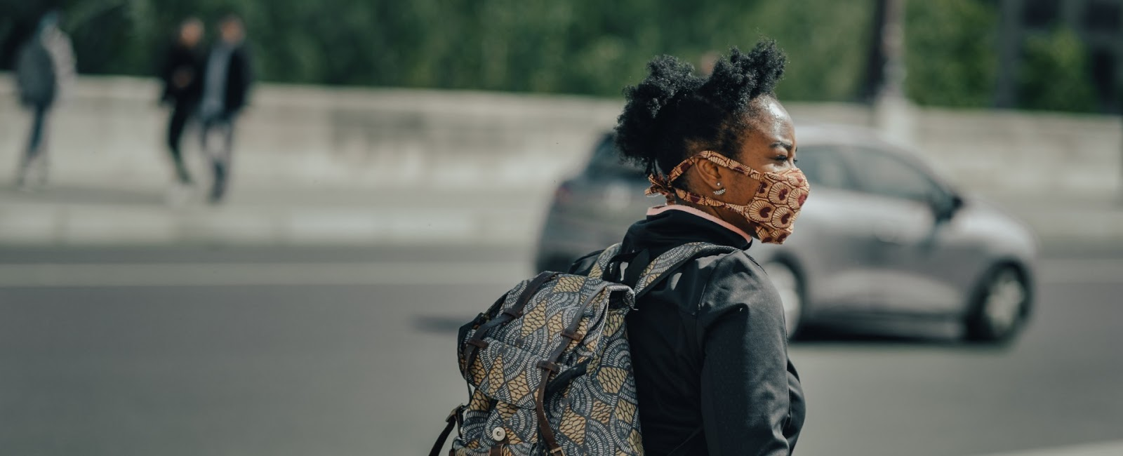 A woman wearing a mask and a backpack is crossing the street.