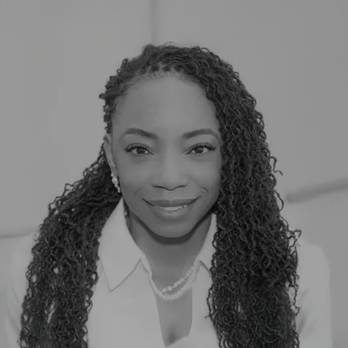 A black and white photo of a woman with curly hair wearing a white shirt and a pearl necklace.