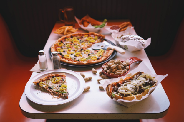 A table topped with plates of food including a pizza and a hot dog A table topped with plates of food including a pizza and a hot dog