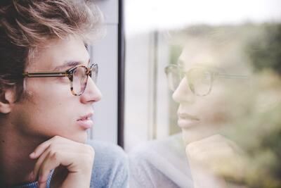 A young man wearing glasses is looking out of a window. A young man wearing glasses is looking out of a window.