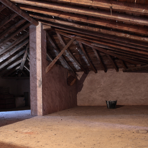 Interior of an old barn with wooden beams, pale pink walls, and a dirt floor.