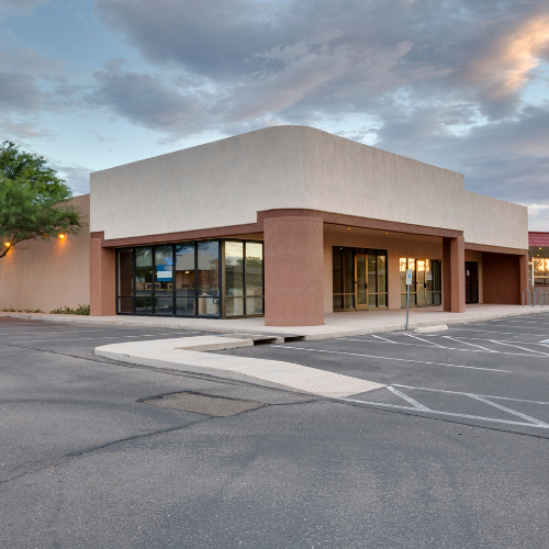 A one-story commercial building with tan and brown exterior, large windows, and an empty parking lot.