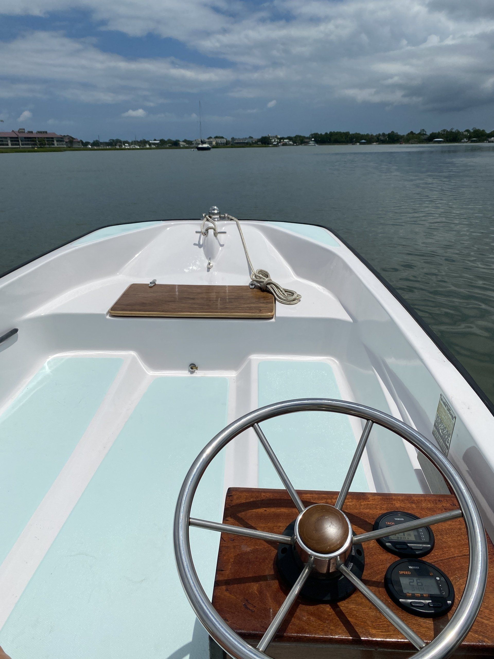 The front of a boat with a steering wheel in the foreground