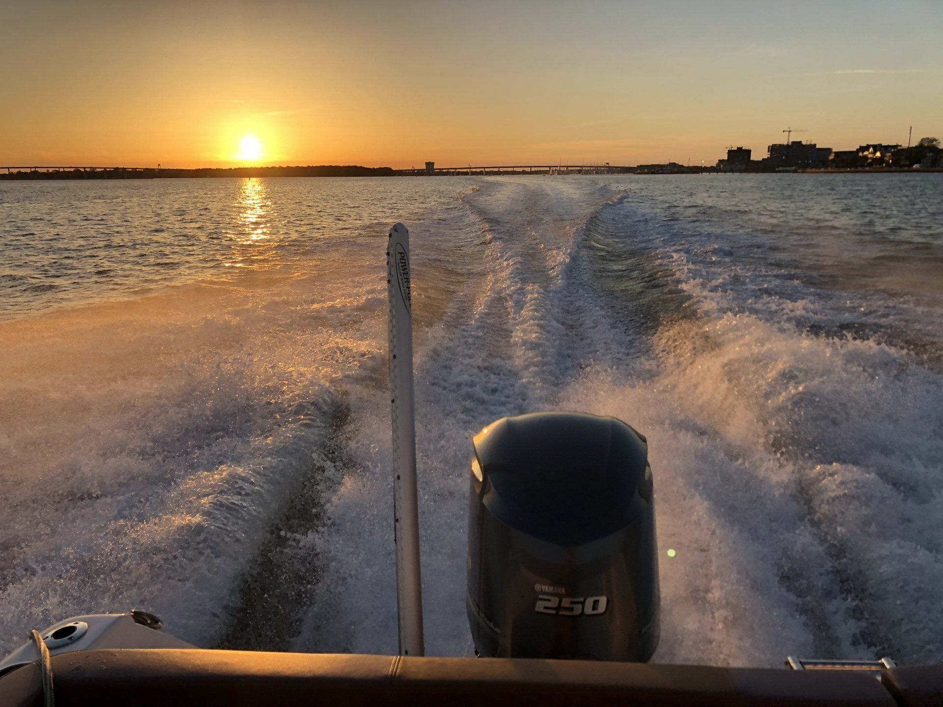 A boat is going through the water with the sun setting in the background
