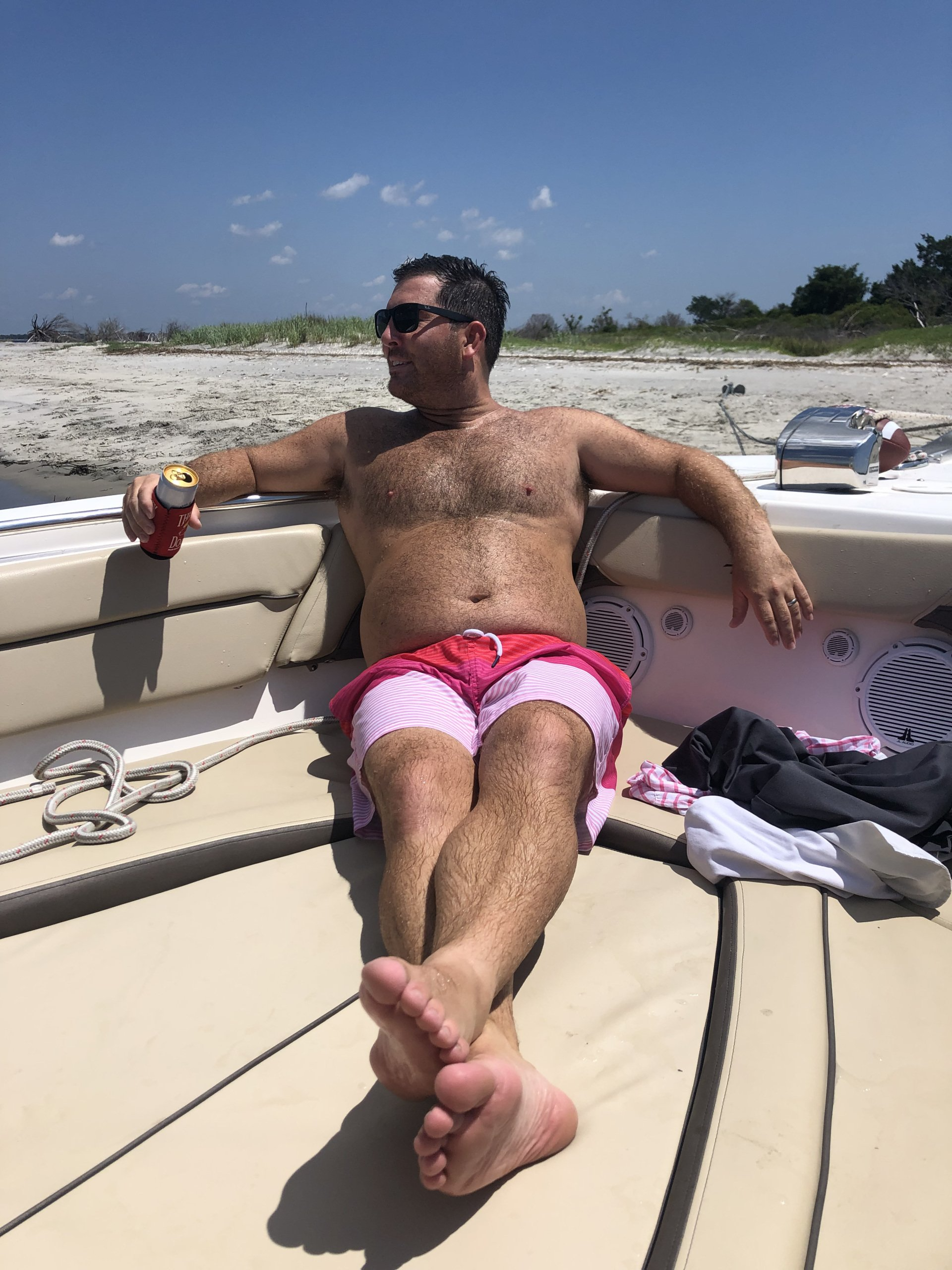 A shirtless man is sitting on a boat holding a can of soda.