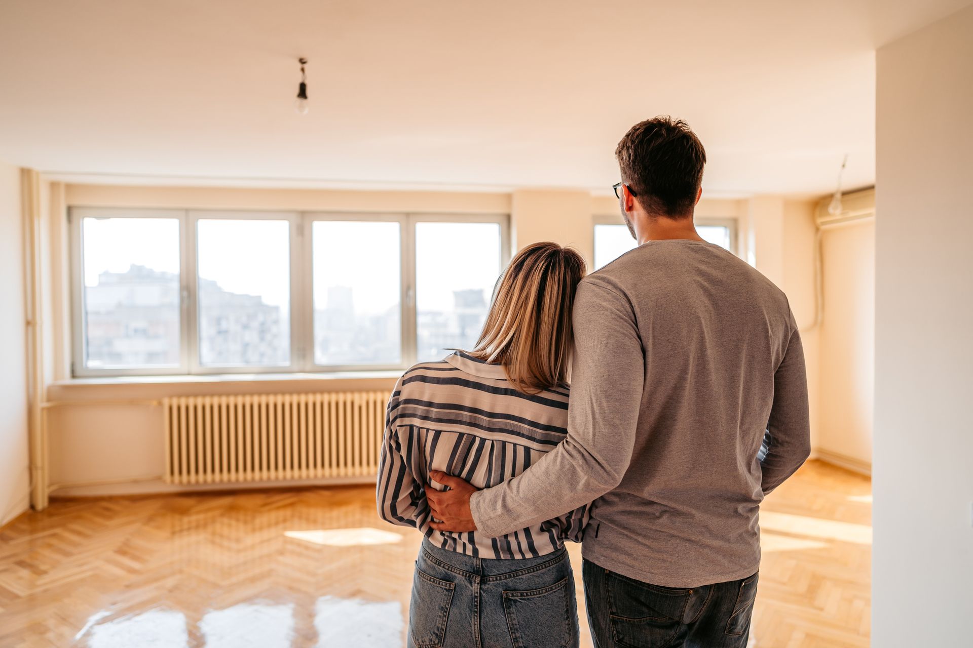 A man and a woman are standing in an empty room looking out the window.