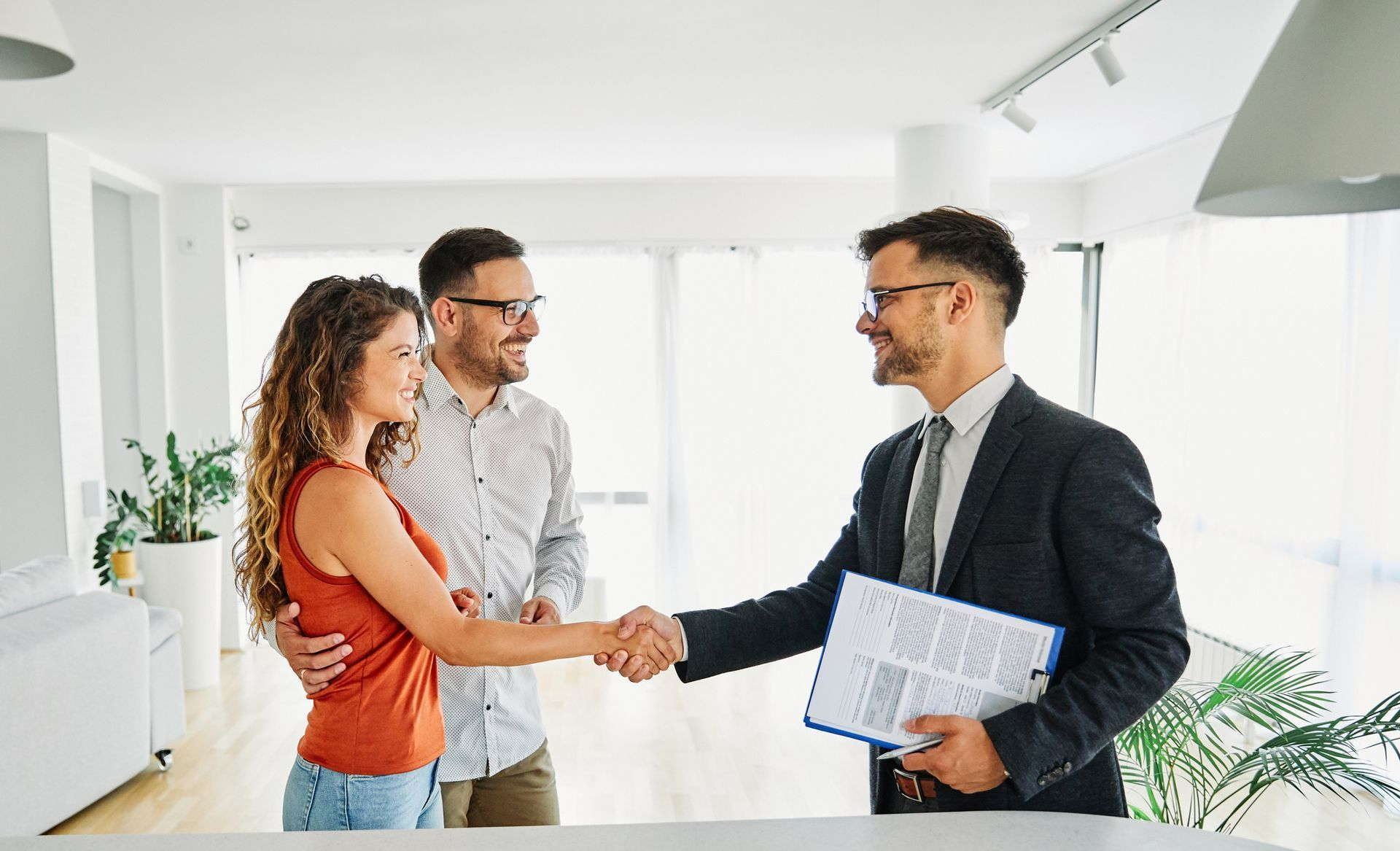 A man and woman are shaking hands with a real estate agent in a living room.