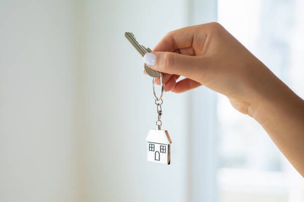 A woman is holding a key with a house keychain attached to it.