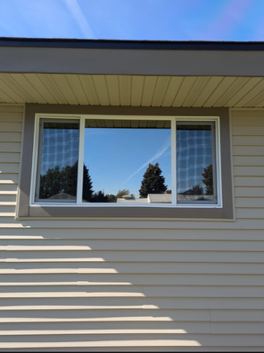 A window on the side of a house with trees reflected in it