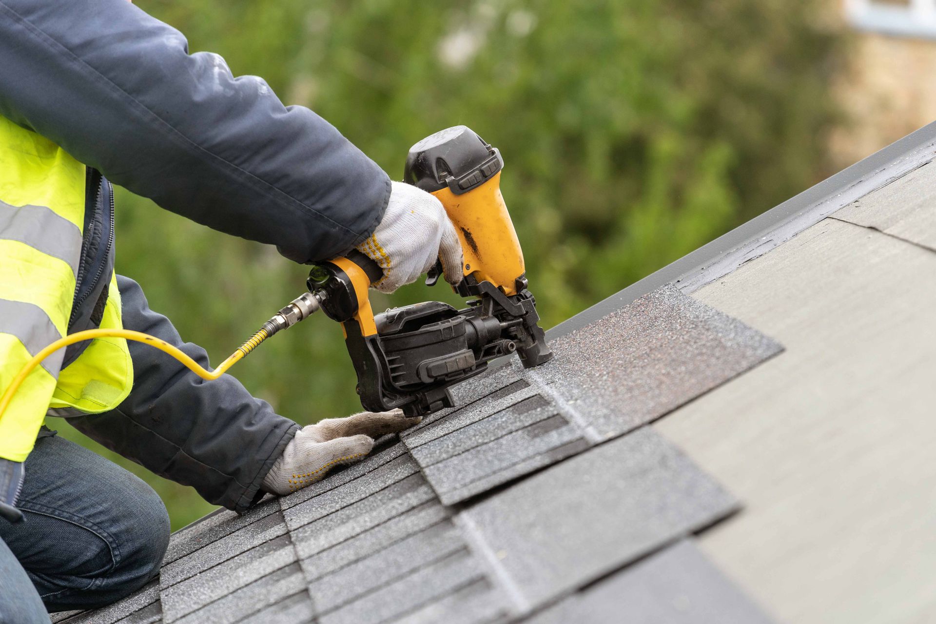 Worker using a nail gun to install shingles during a roof replacement, ensuring durability.