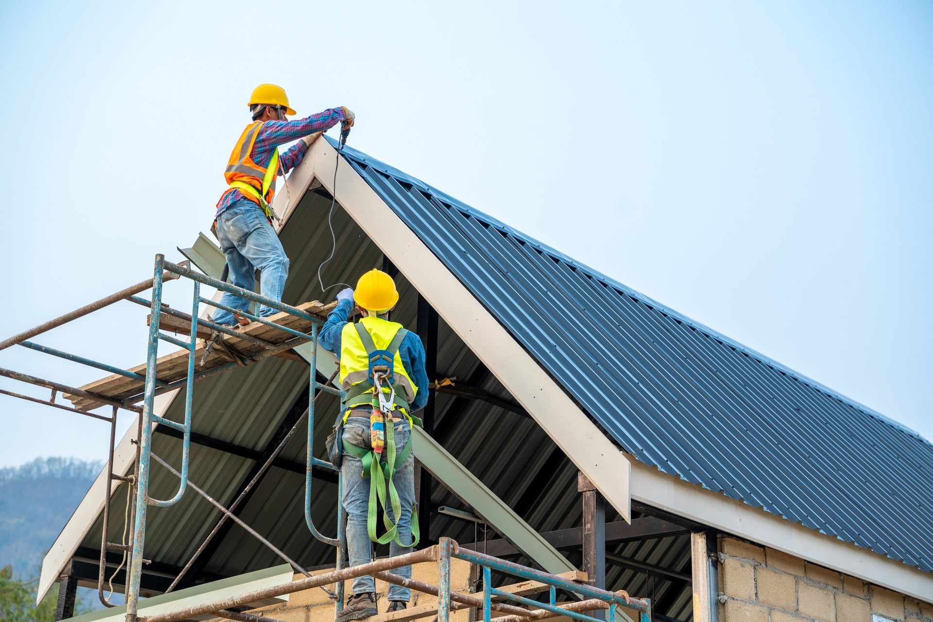 Roofing contractors wearing protective gear and working on roof metal cheese in construction site.]
