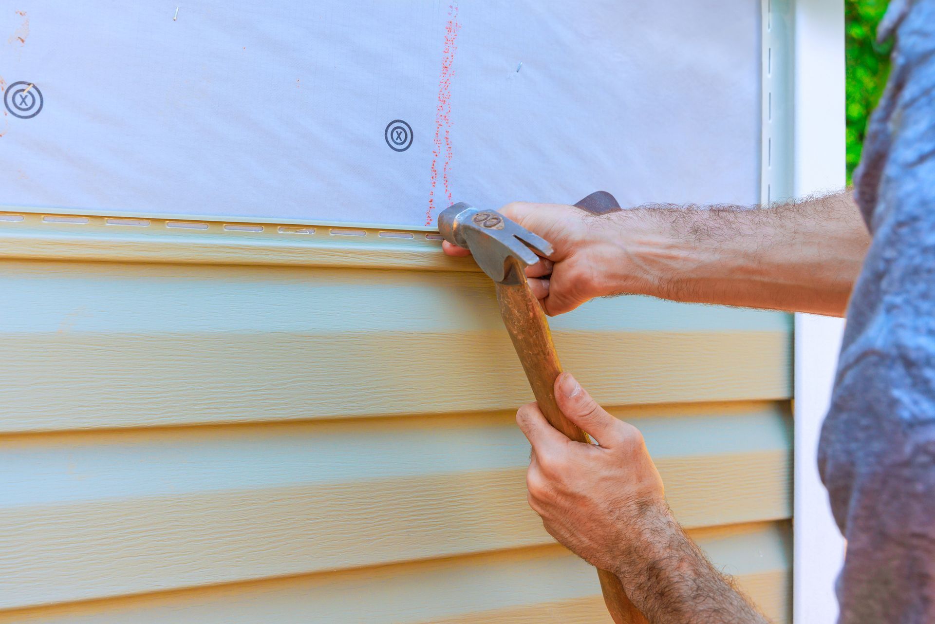 Worker is using hammer to secure new PVC vinyl siding. Worker is using hammer to secure new PVC vinyl siding.
