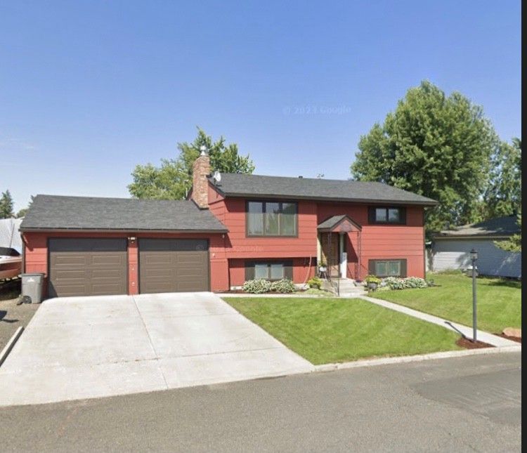Red two-story house with a two-car garage, concrete driveway, and a small front lawn.