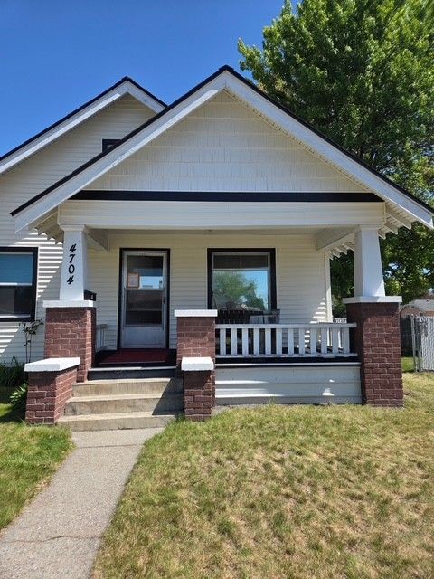 Small white house with a front porch, brick columns, and a concrete walkway leading to the steps