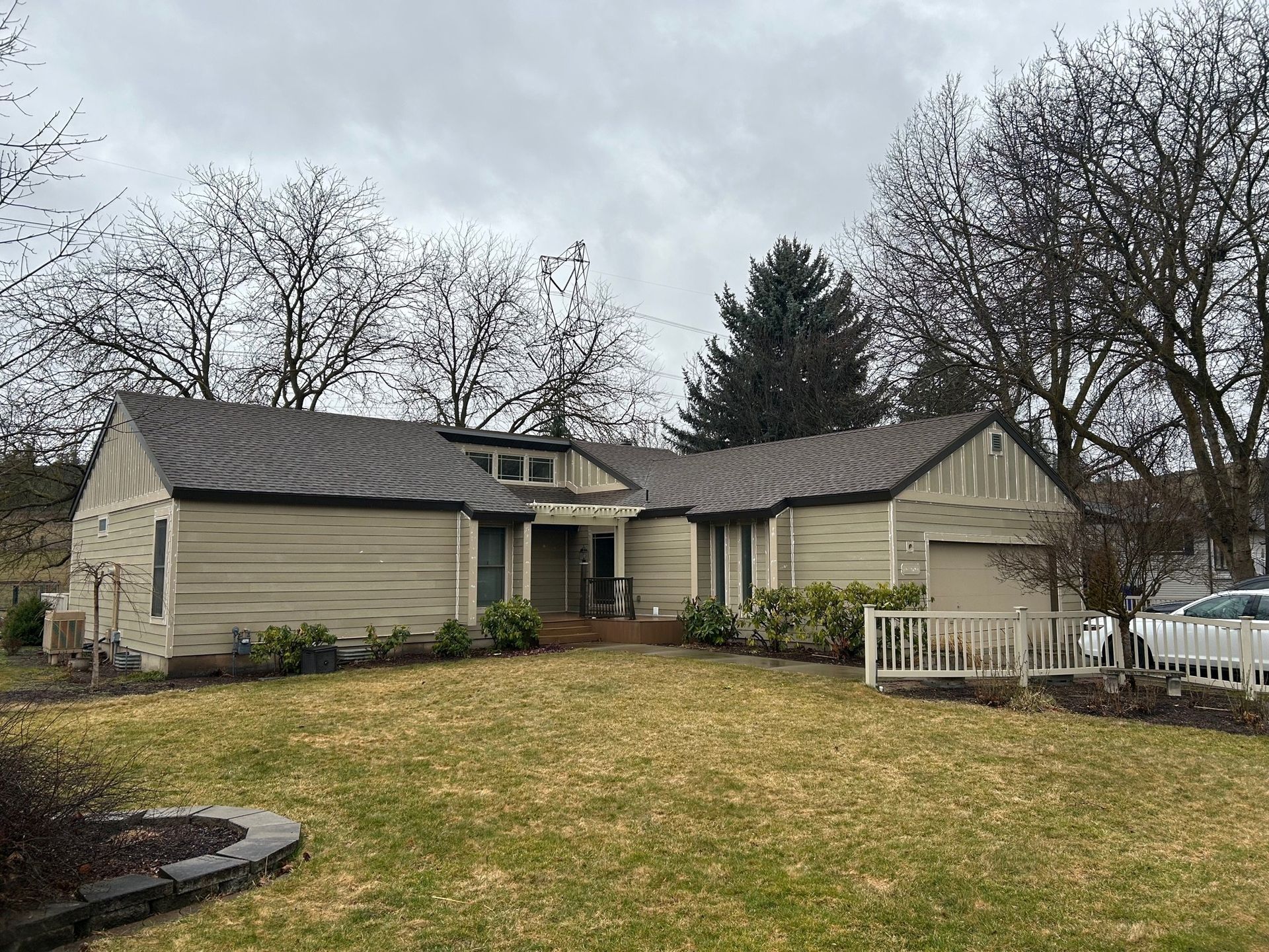 A beige ranch-style house with a brown roof and a small front yard on a cloudy day.