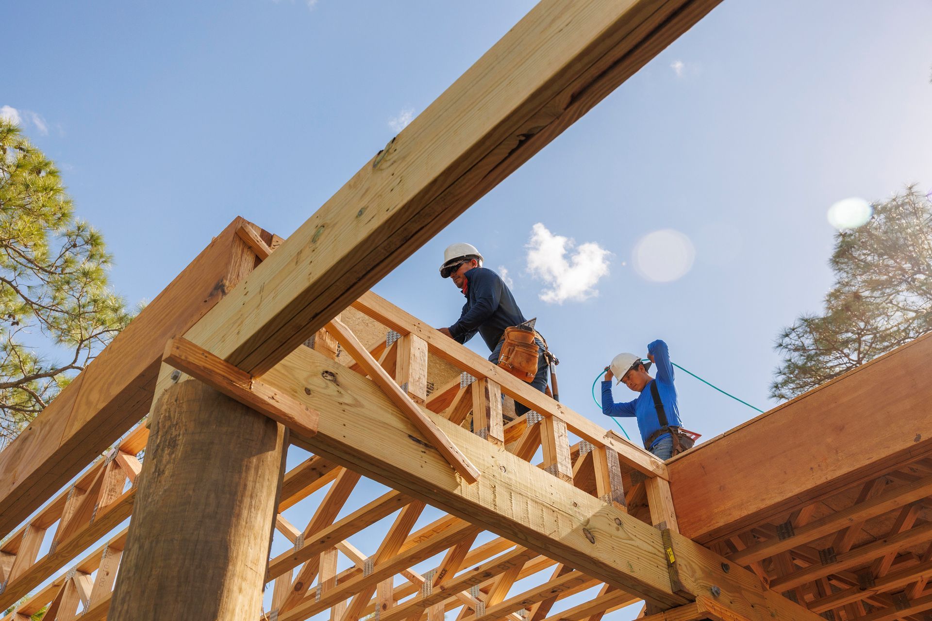Low-angle view of two male roofing contractors as they work on the wooden frame of a roof.